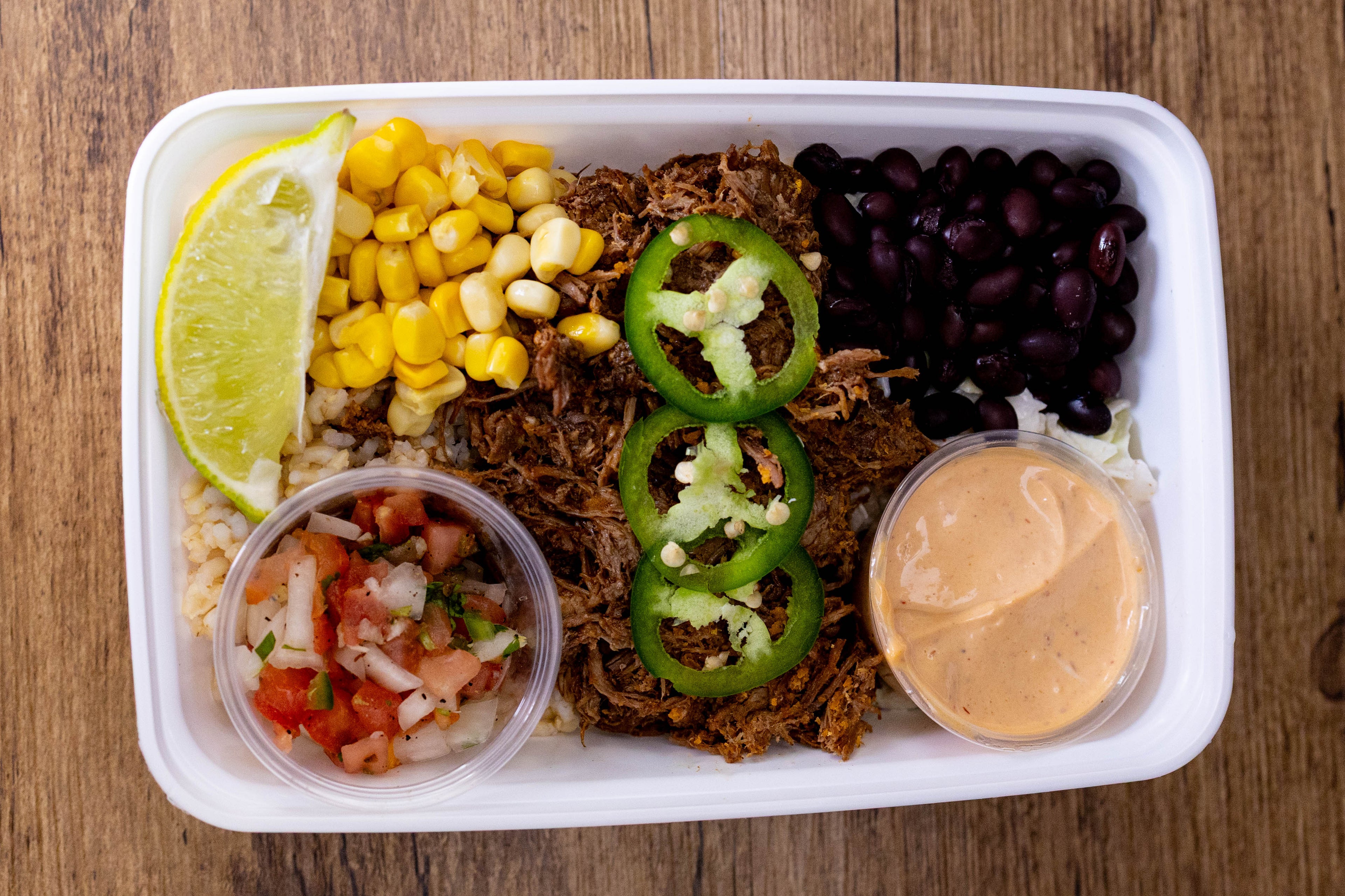 Freshly prepared burrito bowl with shredded beef, corn, black beans, jalapeños and sauces, highlighting healthy options from meal prep services.